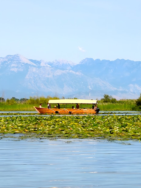 Wooden boat on Lake Skadar during guided sightseeing tour with mountain backdrop.