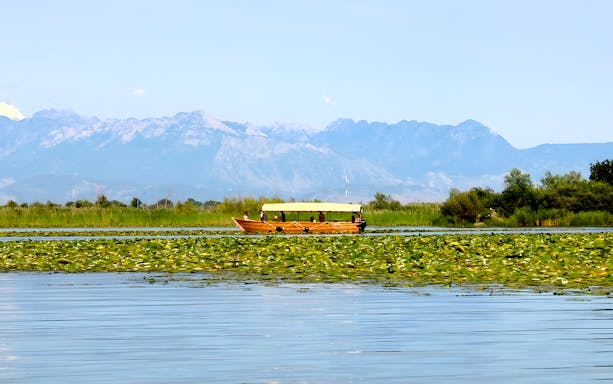 Wooden boat on Lake Skadar during guided sightseeing tour with mountain backdrop.