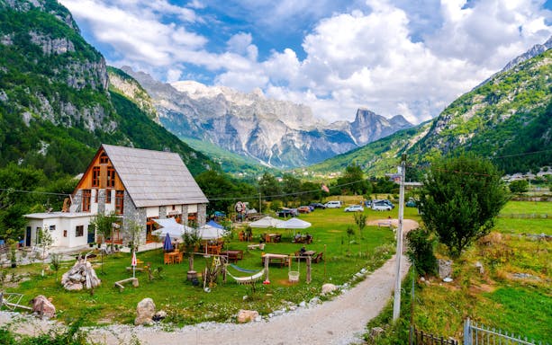 Mountain lodge and outdoor seating in Valley of Theth, Albania, with scenic mountain backdrop.