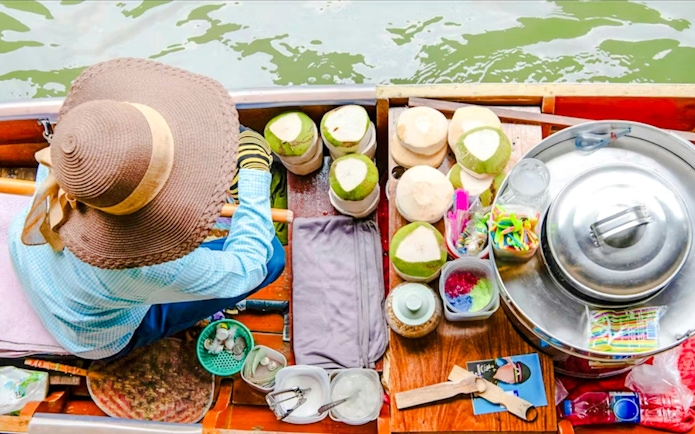 Woman selling coconuts from a boat at Damnoen Saduak Floating Market, Thailand.