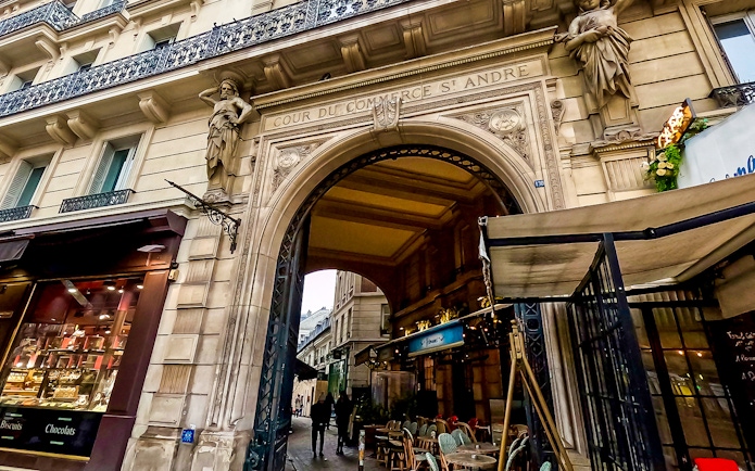 Cour du Commerce Saint-André entrance in Saint-Germain-Des-Prés, Paris, with nearby café tables.