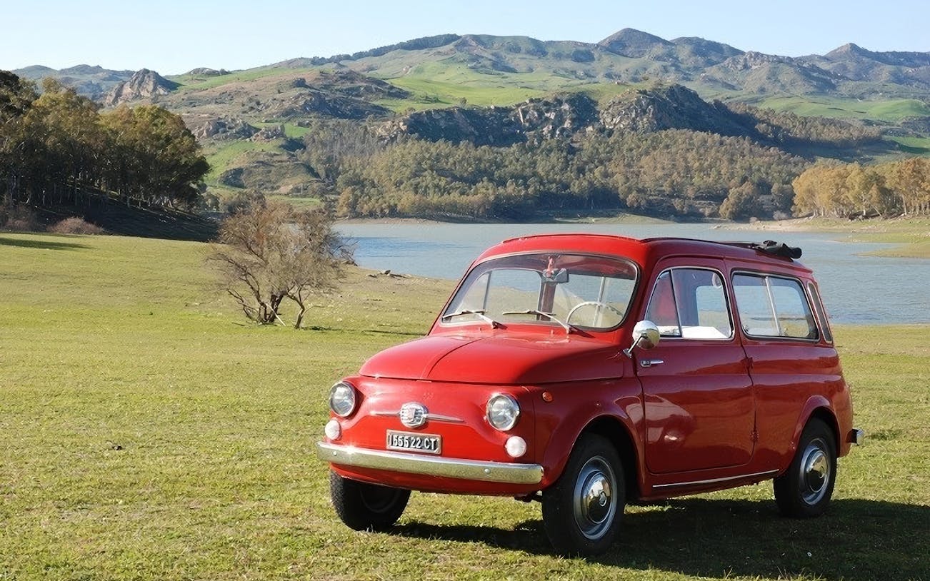 Fiat 500 parked by a scenic lake with mountains in the background.