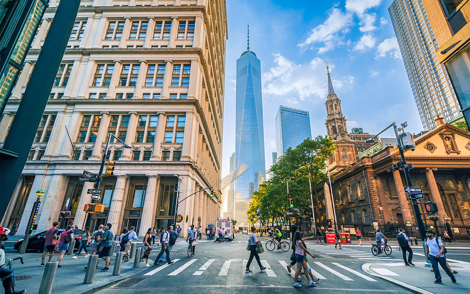 Pedestrians crossing at Fulton and Broadway with skyscrapers in Manhattan, New York City.
