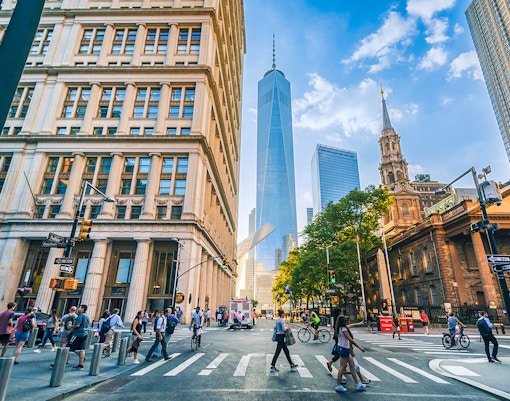 Pedestrians crossing at Fulton and Broadway with skyscrapers in Manhattan, New York City.