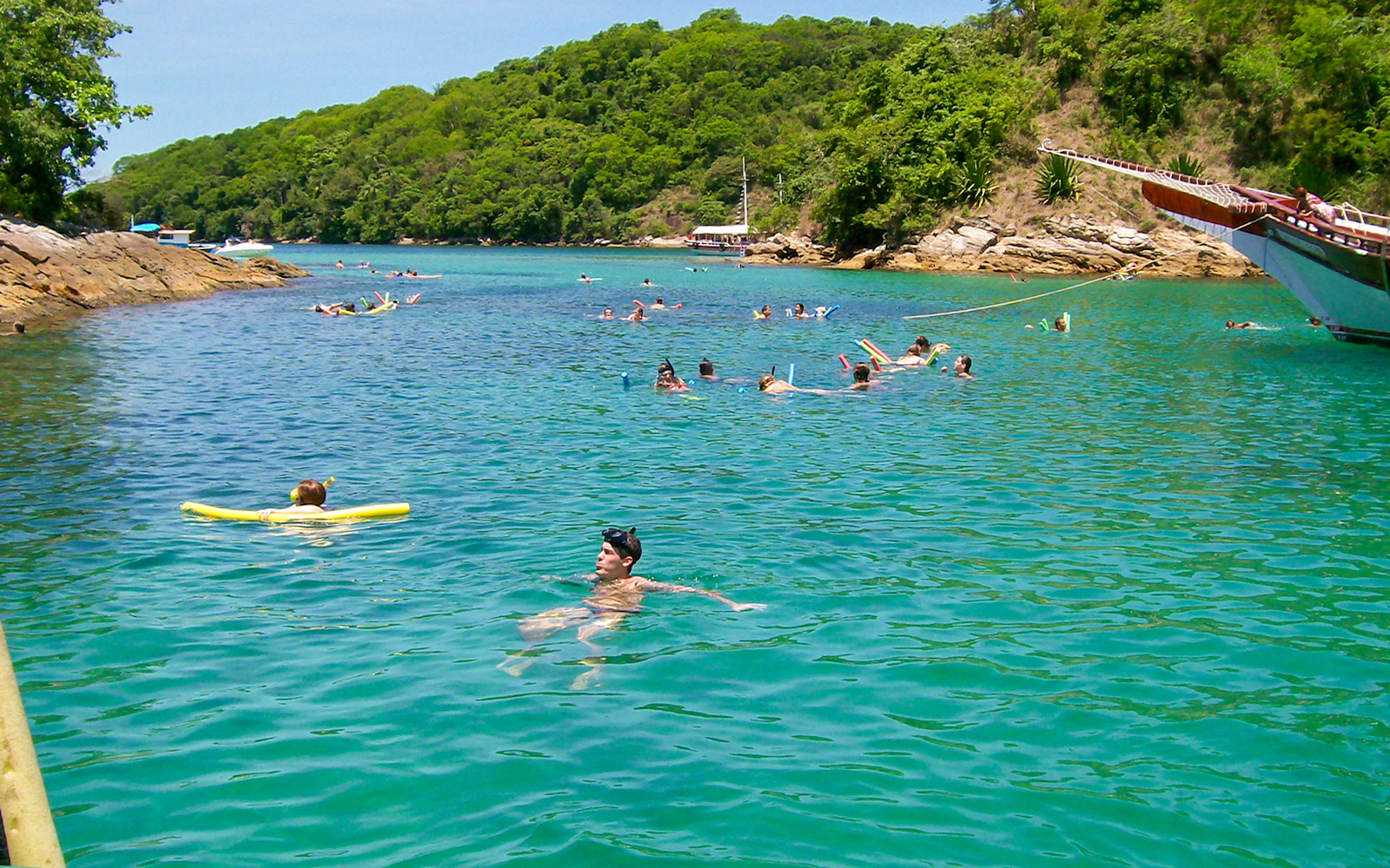 Tourists swimming in clear waters at Japariz Beach, Brazil, surrounded by lush greenery.