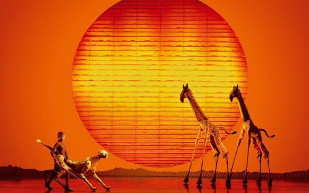 Stage performance of The Lion King with actors as animals against a sunset backdrop.