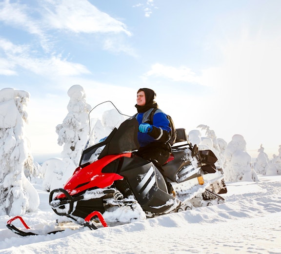 Man driving snowmobile through snowy forest in Lapland.