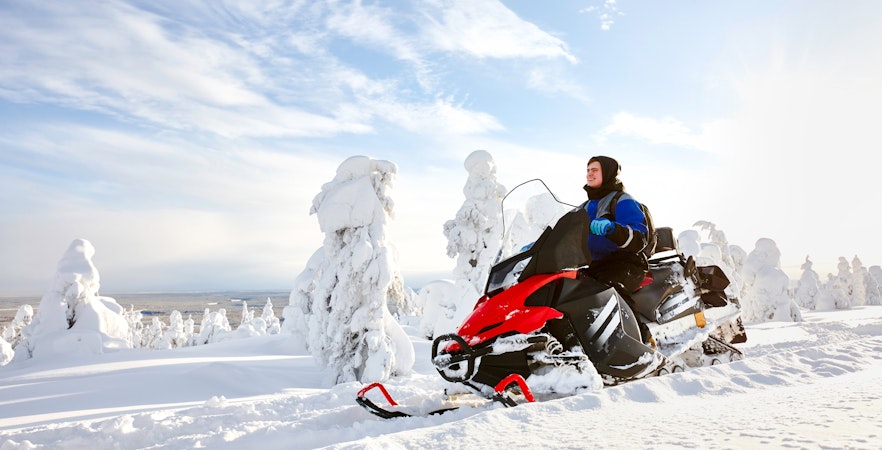 Man driving snowmobile through snowy forest in Lapland.