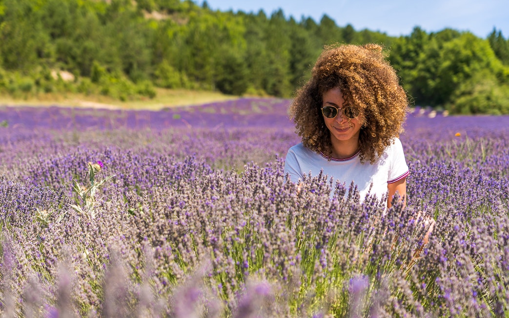 Woman enjoying a lavender field with trees in the background.