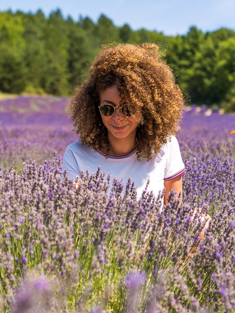Woman enjoying a lavender field with trees in the background.