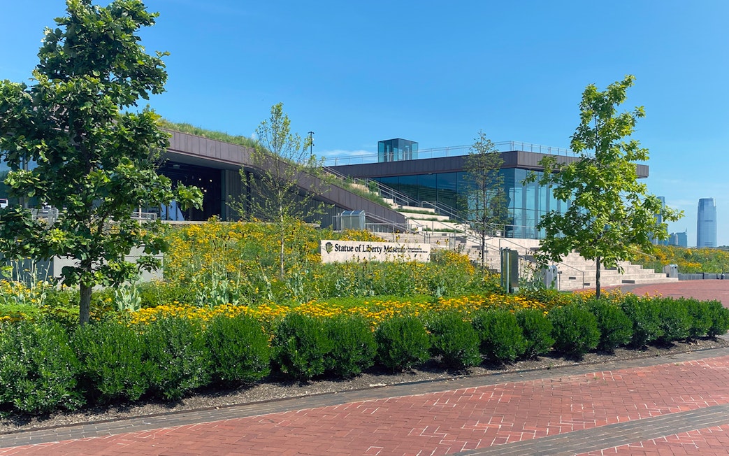 Statue of Liberty Museum entrance with garden and city skyline in the background.