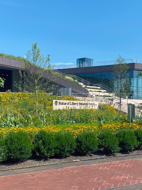 Statue of Liberty Museum entrance with garden and city skyline in the background.