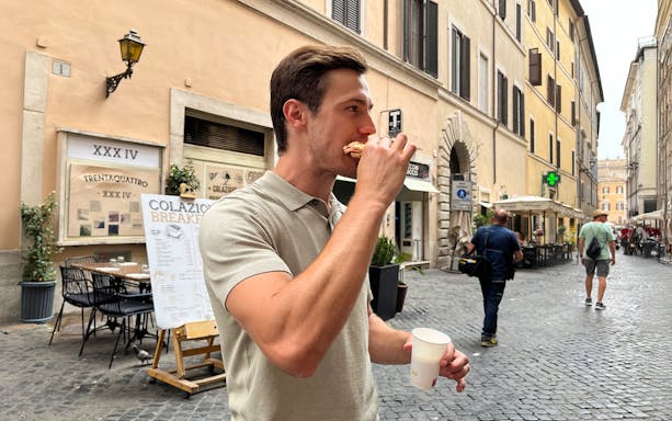 Man enjoying a snack on a cobblestone street in Rome during an evening food tour.