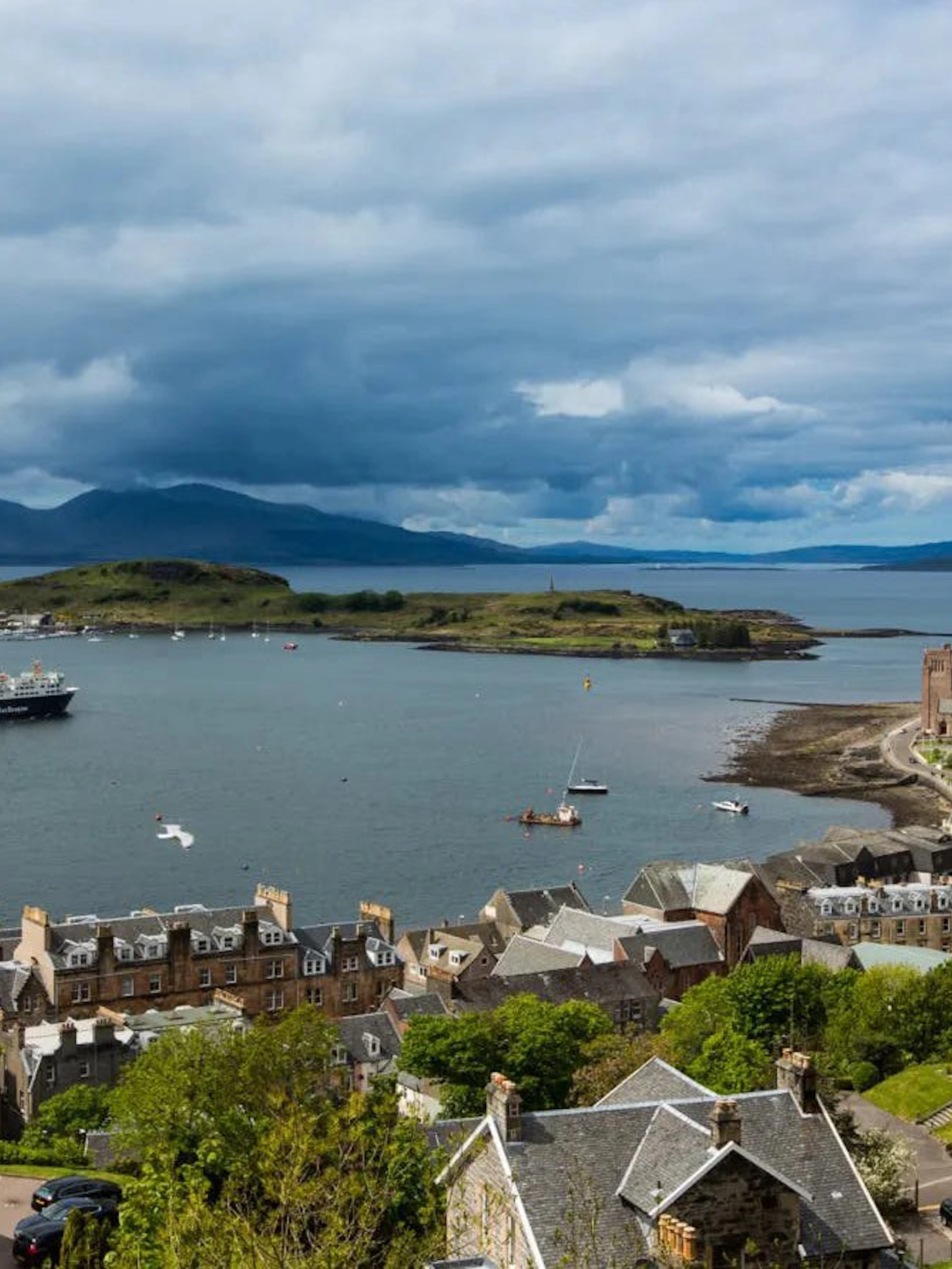 Ferry approaching Oban harbor with coastal town and distant hills in view.