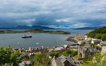 Ferry approaching Oban harbor with coastal town and distant hills in view.