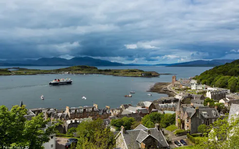 Ferry approaching Oban harbor with coastal town and distant hills in view.