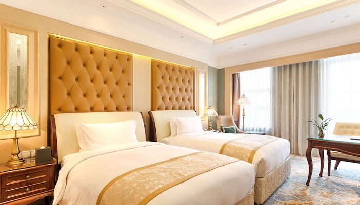 hotel room with two twin beds, each adorned with white linens and a decorative gold-patterned runner.