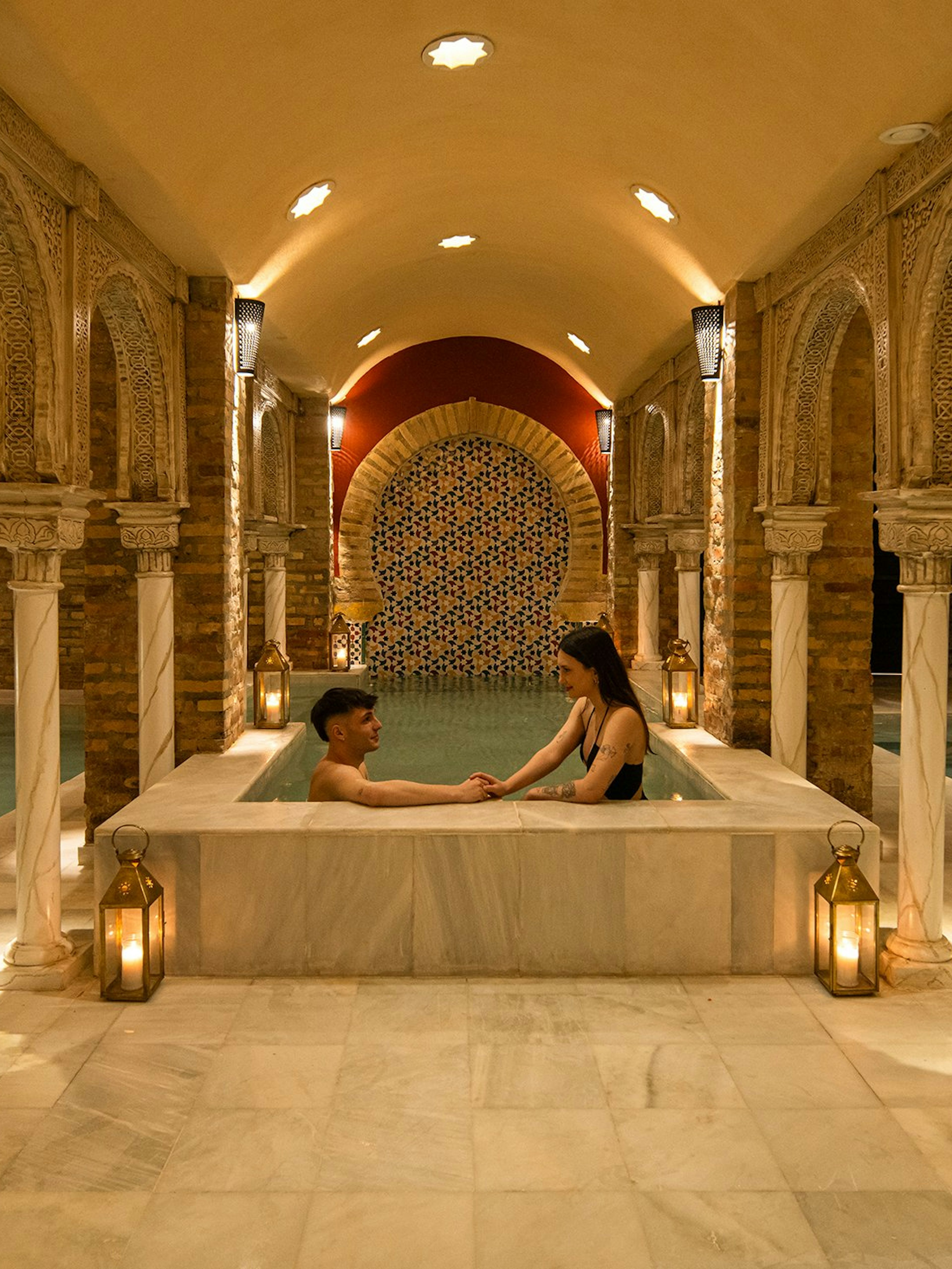 Visitors enjoying a traditional Hammam bath in Granada with ornate arches and warm lighting.
