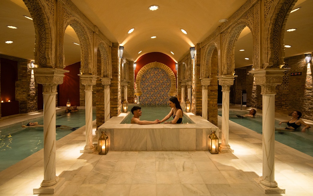 Visitors enjoying a traditional Hammam bath in Granada with ornate arches and warm lighting.