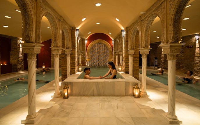 Visitors enjoying a traditional Hammam bath in Granada with ornate arches and warm lighting.