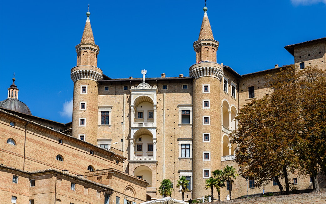 Facade of Ducal Palace in Urbino with twin towers and arched windows.