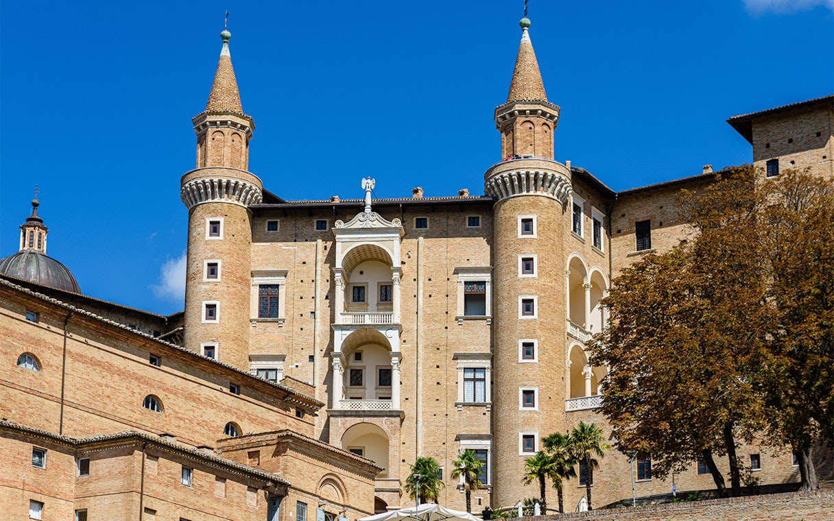 Facade of Ducal Palace in Urbino with twin towers and arched windows.