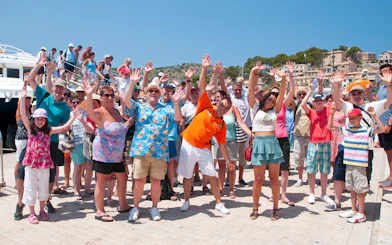 Group of tourists waving near a boat in Mallorca during sightseeing tour.