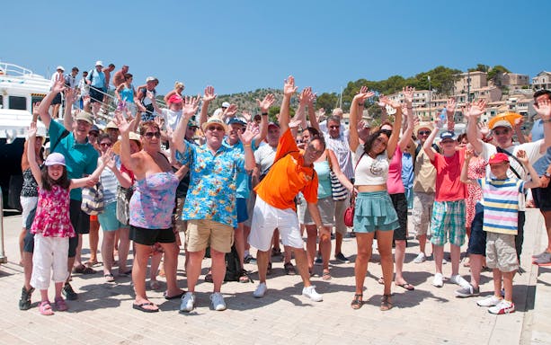 Group of tourists waving near a boat in Mallorca during sightseeing tour.