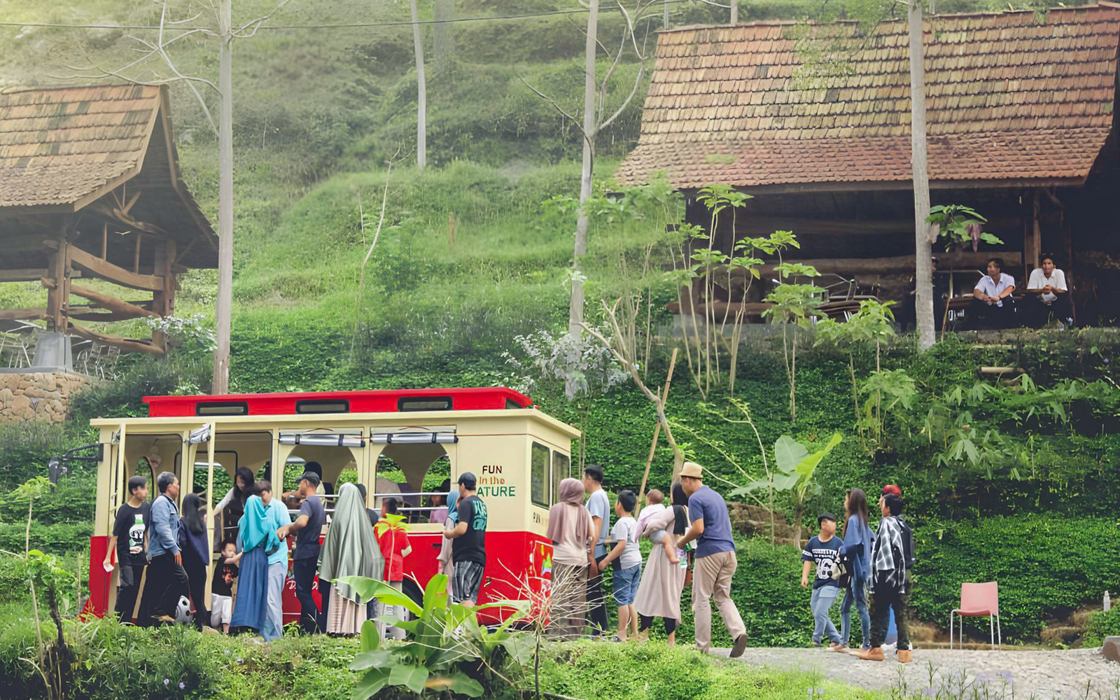 Visitors boarding a red tram at Dago Dreampark, surrounded by lush greenery and traditional huts.