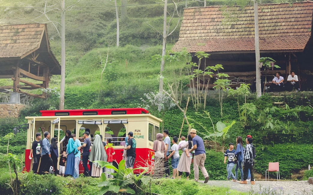 Visitors boarding a red tram at Dago Dreampark, surrounded by lush greenery and traditional huts.