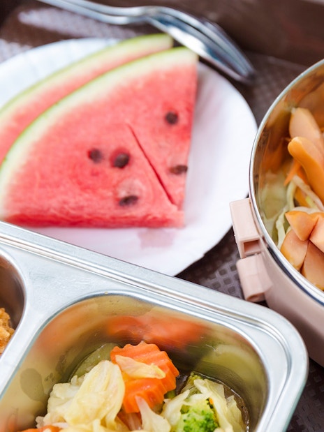 Breakfast buffet with sausages, lettuce, and watermelon slices on a beach setting.