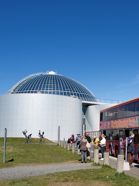 Reykjavik hop-on hop-off bus near Perlan with tourists boarding.