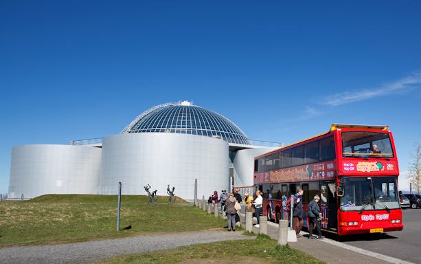 Reykjavik hop-on hop-off bus near Perlan with tourists boarding.