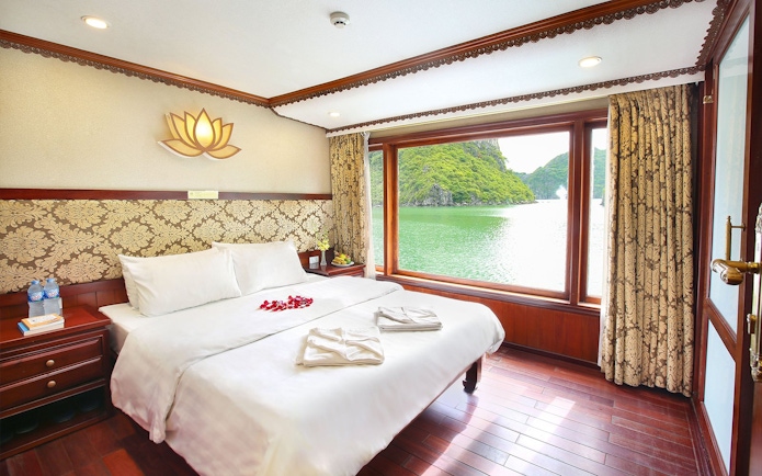 Cruise cabin with large window view of Halong Bay, Vietnam, featuring a double bed and elegant decor.