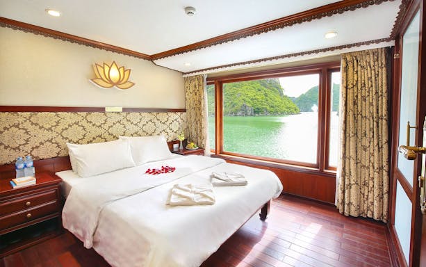 Cruise cabin with large window view of Halong Bay, Vietnam, featuring a double bed and elegant decor.