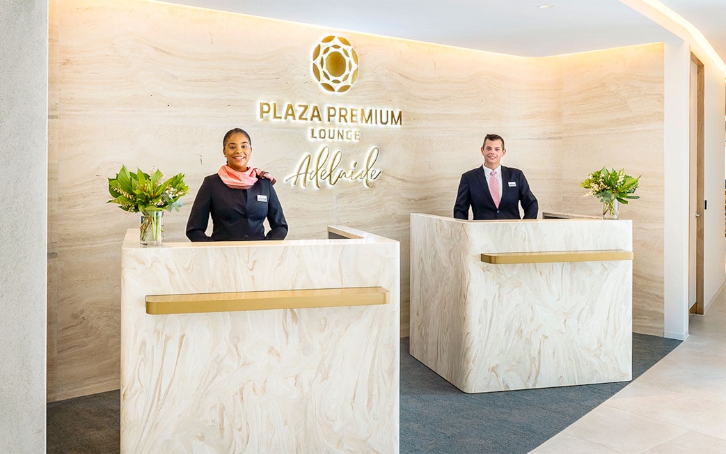 Reception area of Plaza Premium Lounge Adelaide with staff at marble desks.
