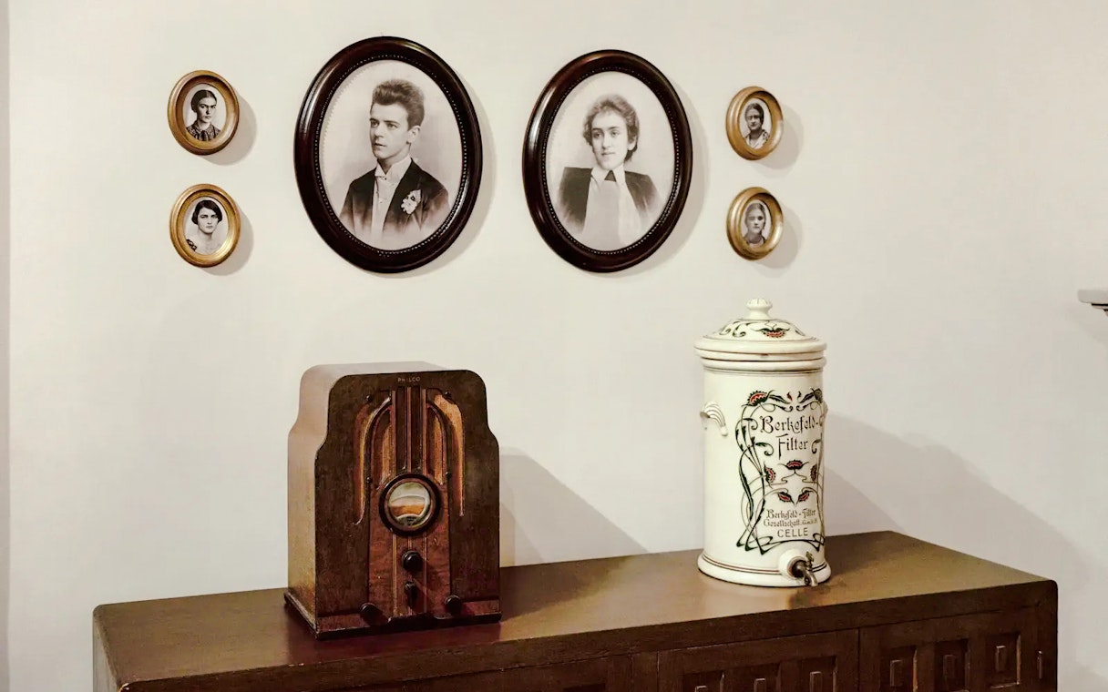 Vintage radio on wooden cabinet with framed portraits on wall.