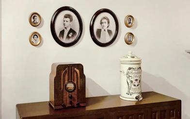 Vintage radio on wooden cabinet with framed portraits on wall.