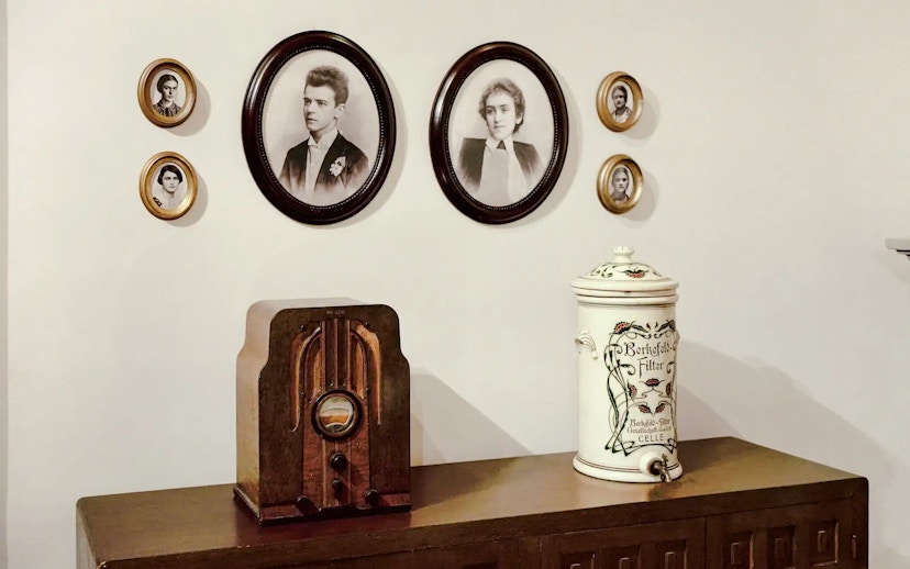 Vintage radio on wooden cabinet with framed portraits on wall.