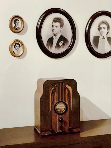 Vintage radio on wooden cabinet with framed portraits on wall.