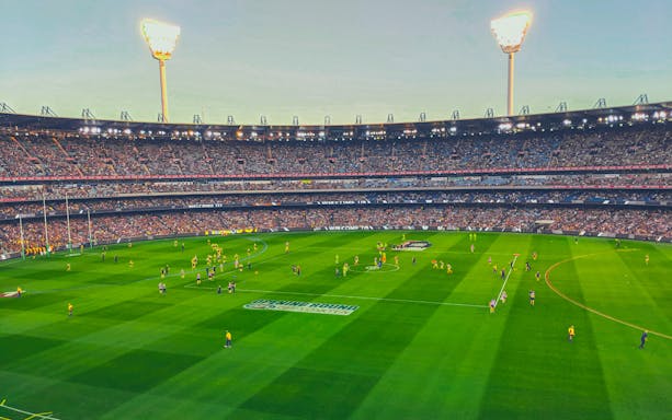 Australian Rules football match at Melbourne Cricket Ground with players on the field.