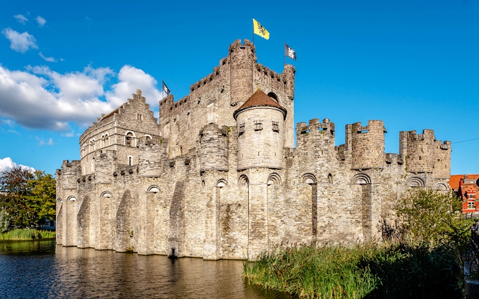 Gravensteen Castle with flags, surrounded by a moat in Ghent, Belgium.