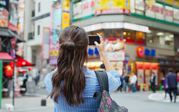 Tourist capturing vibrant Tokyo street scene with cellphone.