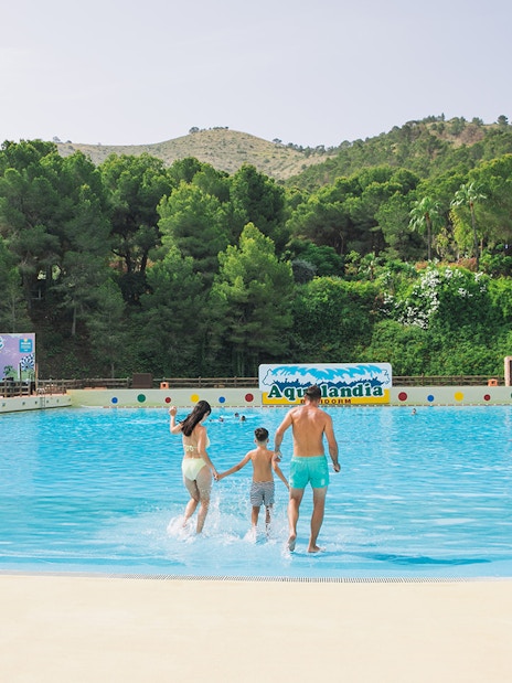 Family entering wave pool at Aqualandia Benidorm with lush greenery in the background.