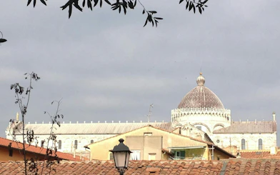 Pisa Cathedral dome viewed over rooftops, part of Pisa Romantic Walk exploration game.