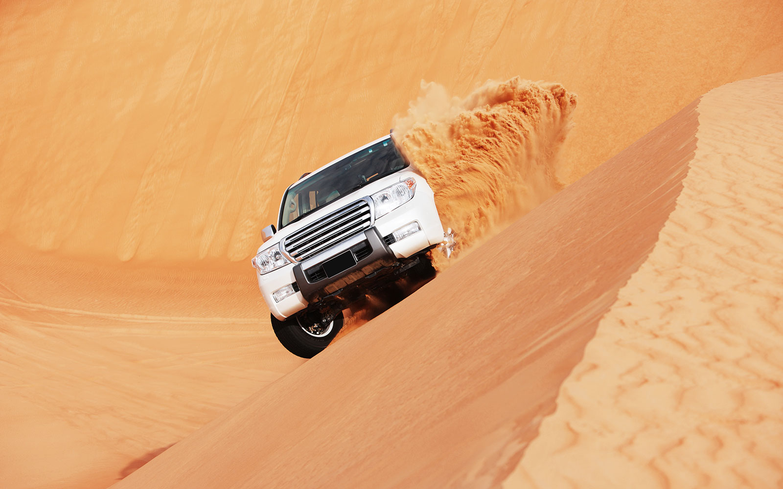 SUV driving on sand dune during dune bashing tour in Doha.