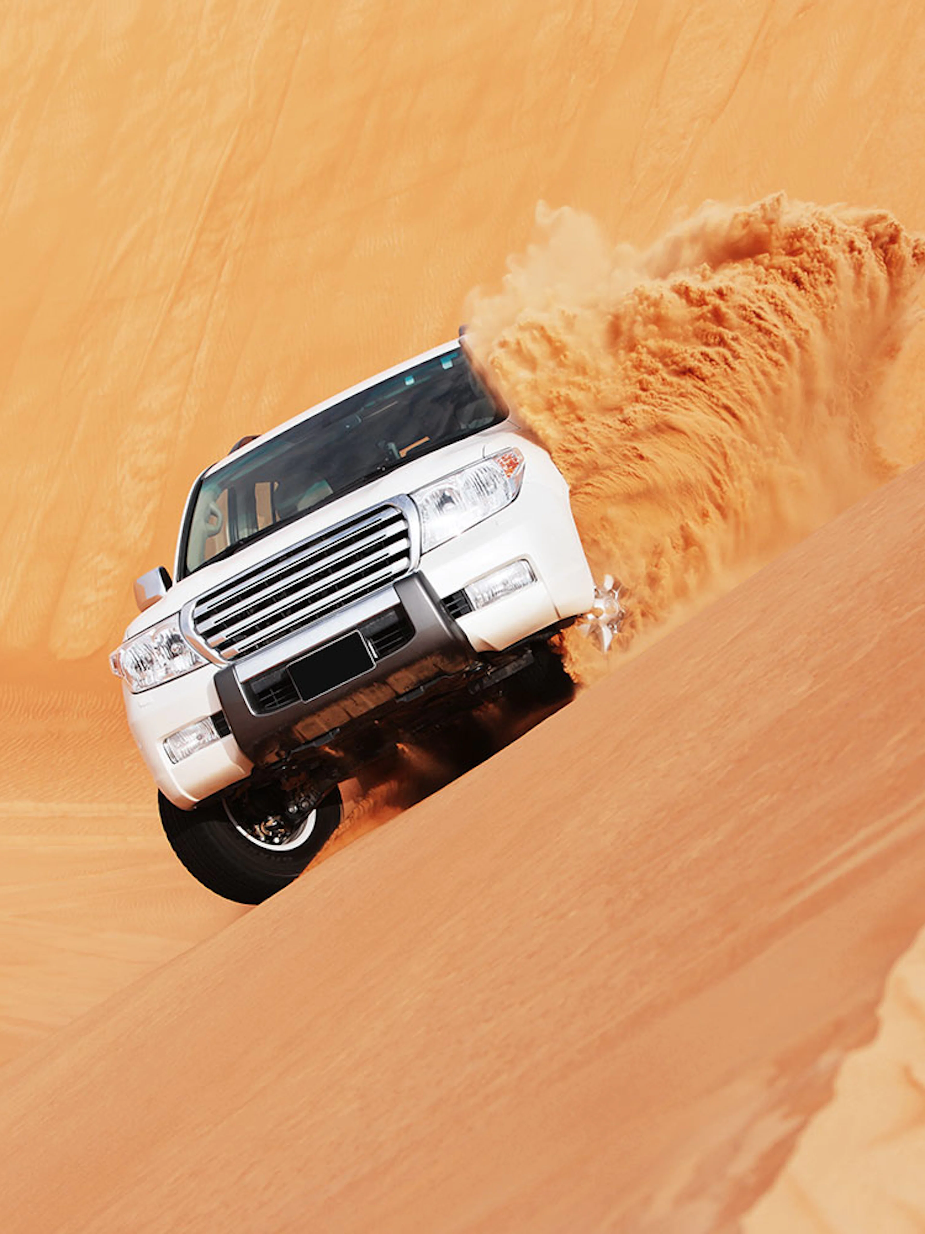 SUV driving on sand dune during dune bashing tour in Doha.