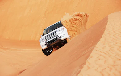 SUV driving on sand dune during dune bashing tour in Doha.