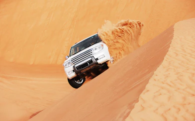 SUV driving on sand dune during dune bashing tour in Doha.