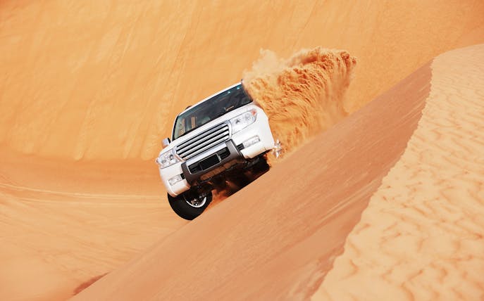 SUV driving on sand dune during dune bashing tour in Doha.